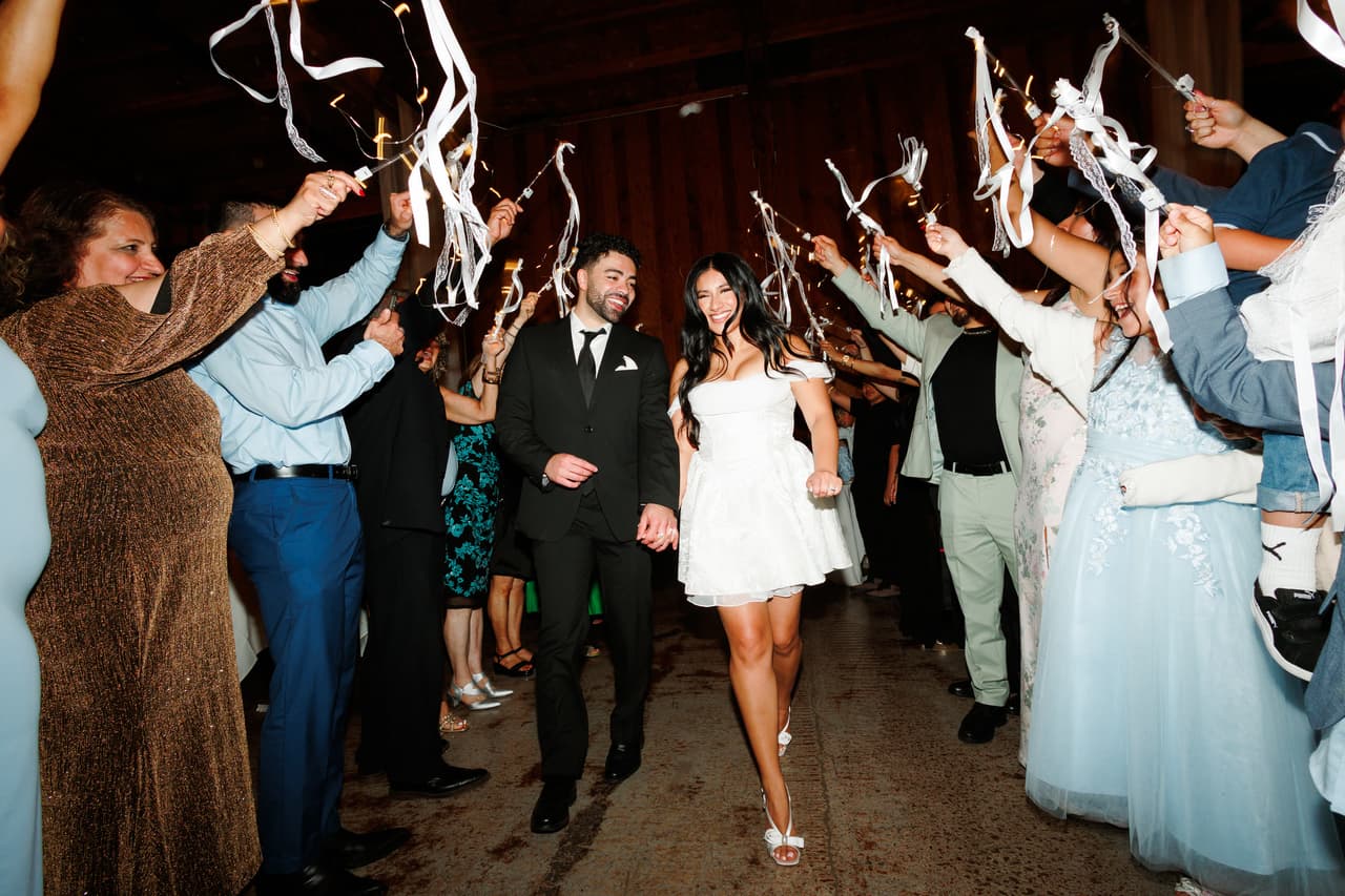 Newlyweds exiting their reception hand in hand through a tunnel of ribbon wands held by guests